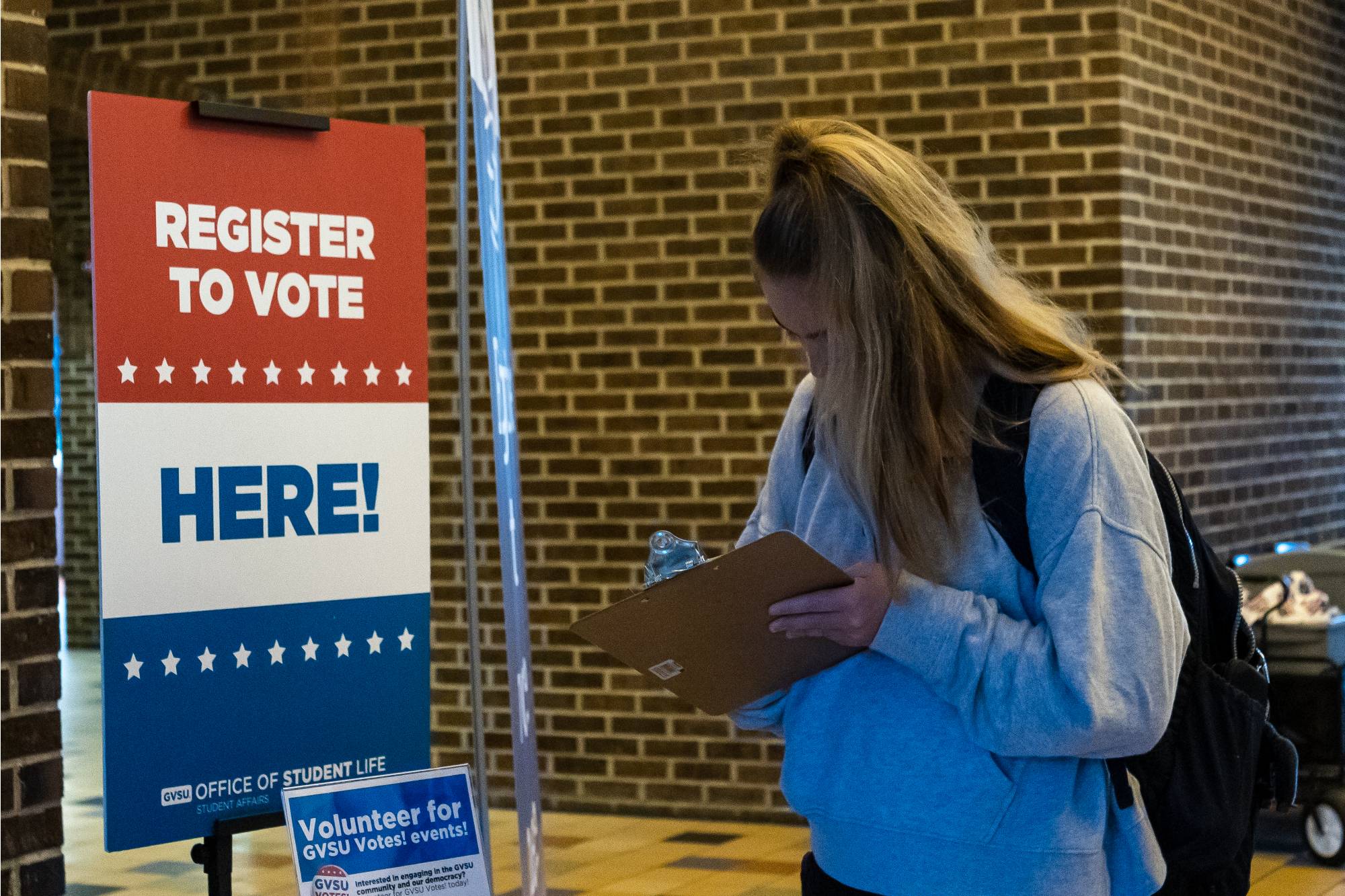 A student registering to vote in front of a register to vote sign